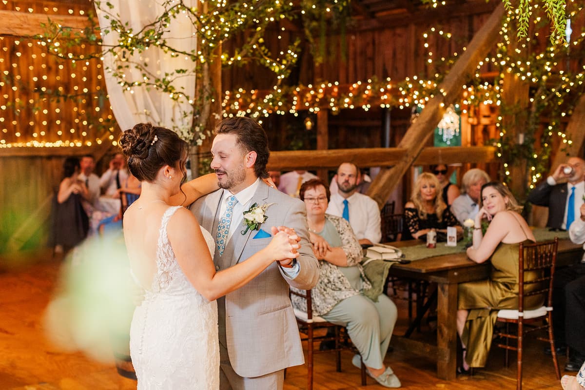 Couple first dance in rustic barn with string lights