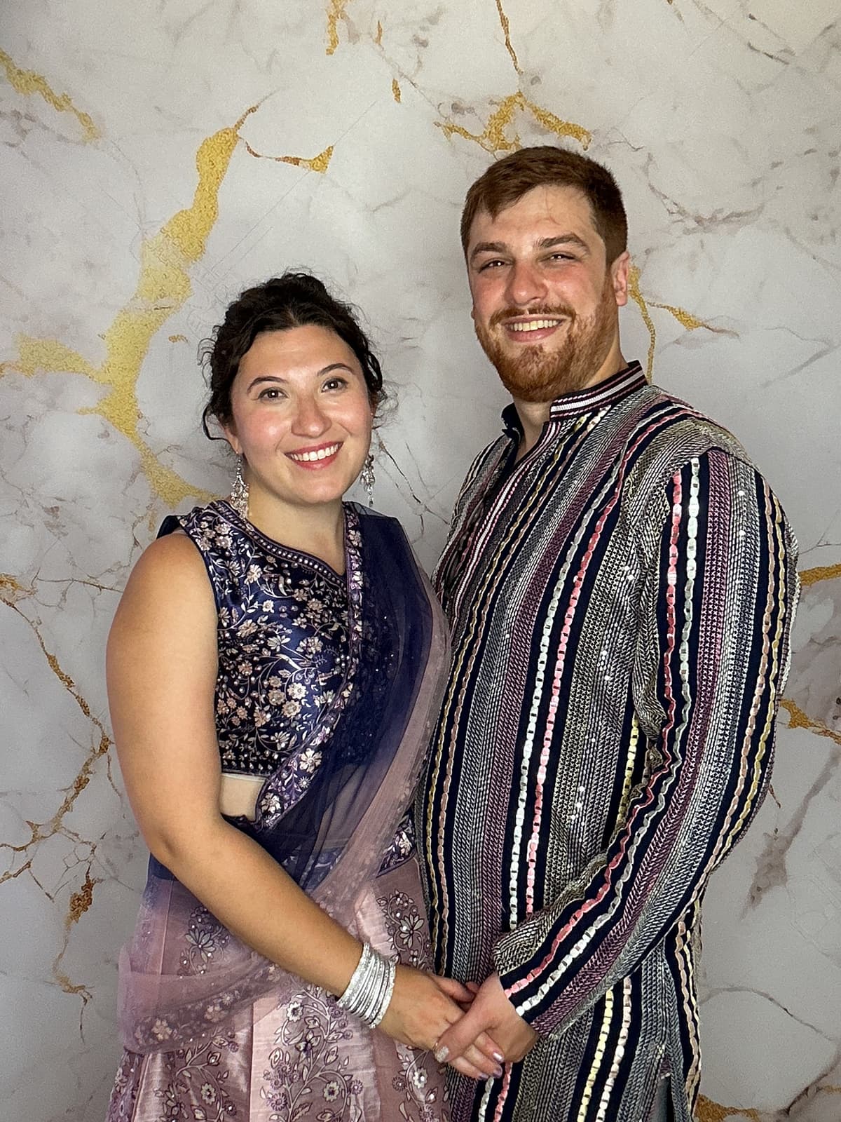 Couple portrait in photo booth - woman in purple lehenga and man in striped kurta with gold marble backdrop